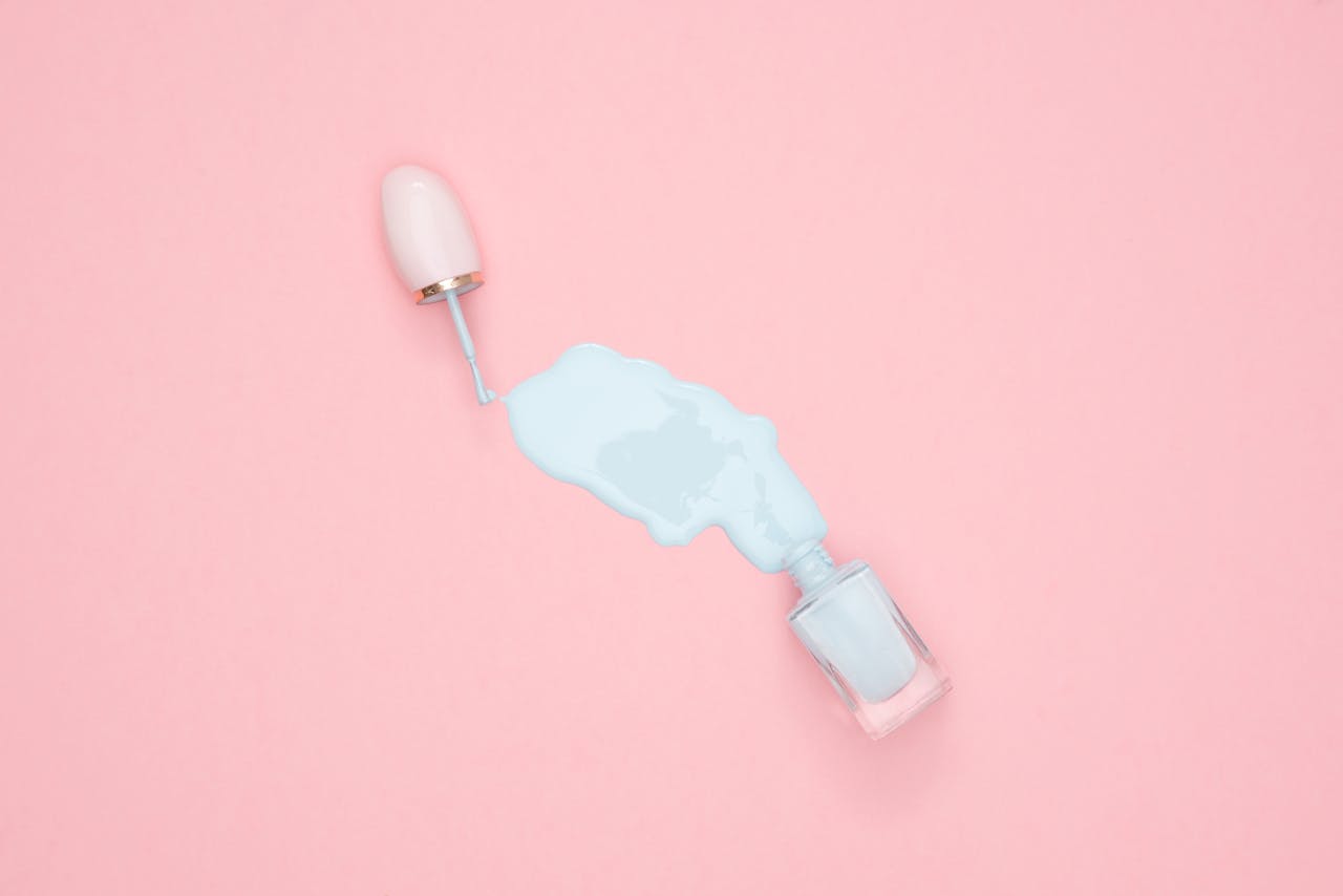 who-we-are Artistic top view of blue nail polish spill on a pink background with copyspace.